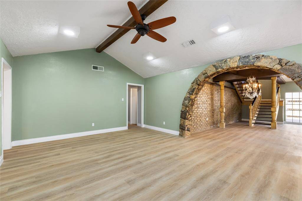 Another angle of the living room highlights the impressive stone arch leading into the formal dining area. Beyond the dining space, a custom-built staircase crafted with high-quality materials draws the eye, while the exposed brick wall and elegant chandelier add warmth and character.