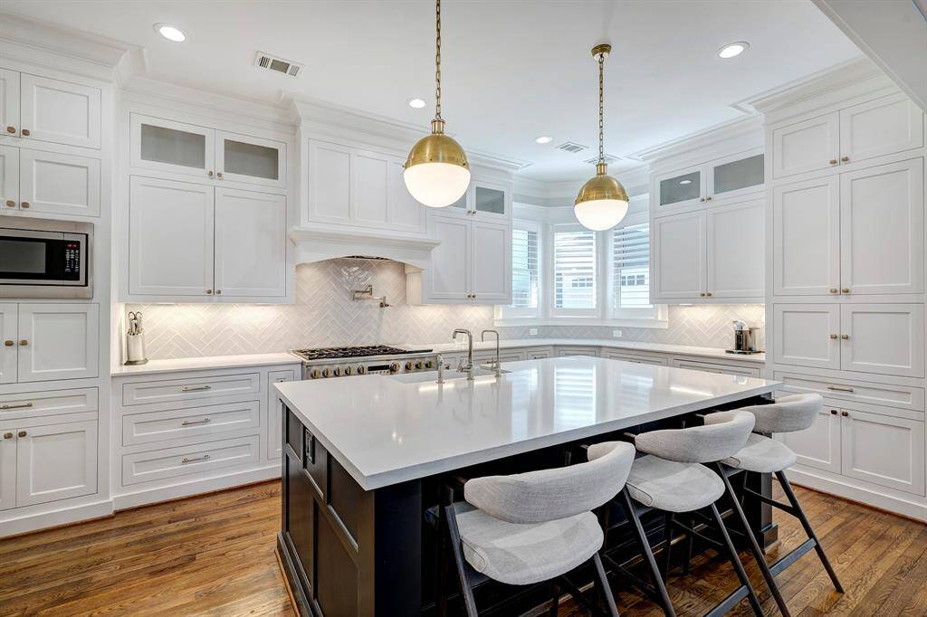 Chef's kitchen featuring a spacious island with farmhouse sink, stylish modern light fixtures, and an abundance of cabinets, and drawers.