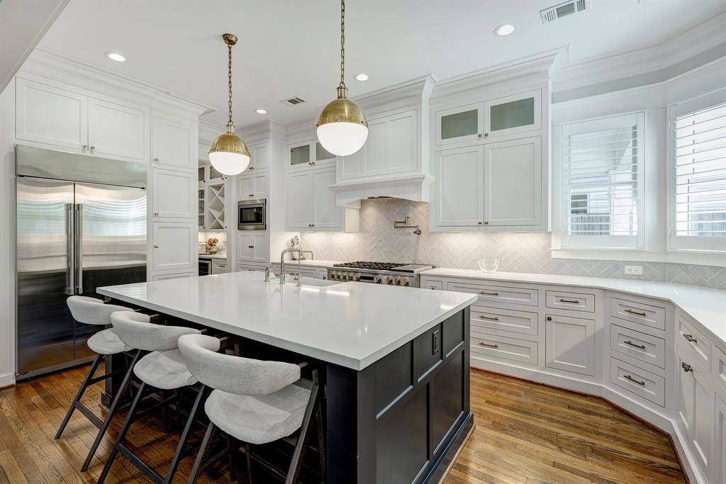 Kitchen island with seating, expansive counter space, a large range with vent hood and pot filler, all accented by a sleek modern backsplash.
