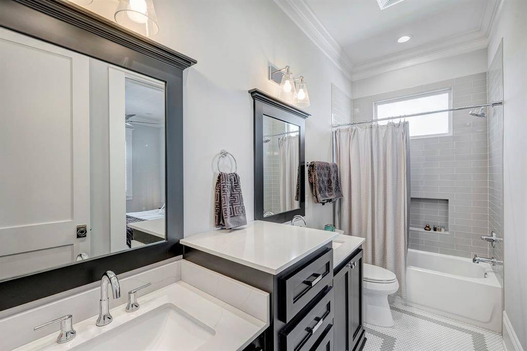 Stylish secondary bathroom featuring dual sinks, a tub/shower combo, ample storage, and modern tile with vintage-inspired charm.