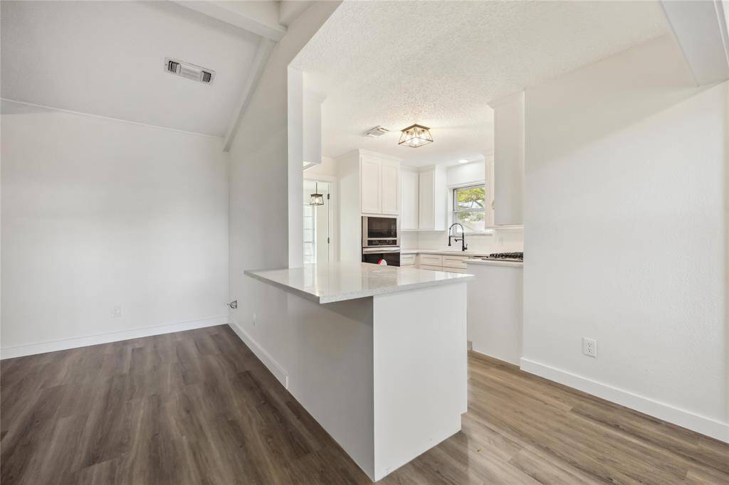 This photo showcases a bright, modern kitchen with white cabinetry, sleek countertops, and stainless steel appliances. The open layout features hardwood floors and a breakfast bar, enhancing the spacious feel.