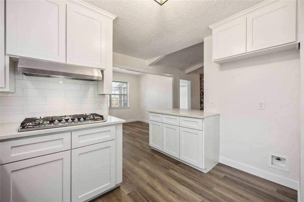 Modern kitchen with sleek white cabinetry, gas cooktop, and stainless steel hood. Features open shelving, a spacious island, and wood-style flooring, creating a bright and inviting space.