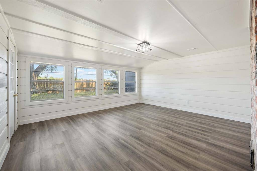 This bright, spacious room features large windows for natural light, white shiplap walls, and sleek wood-look flooring, creating a modern and inviting atmosphere.