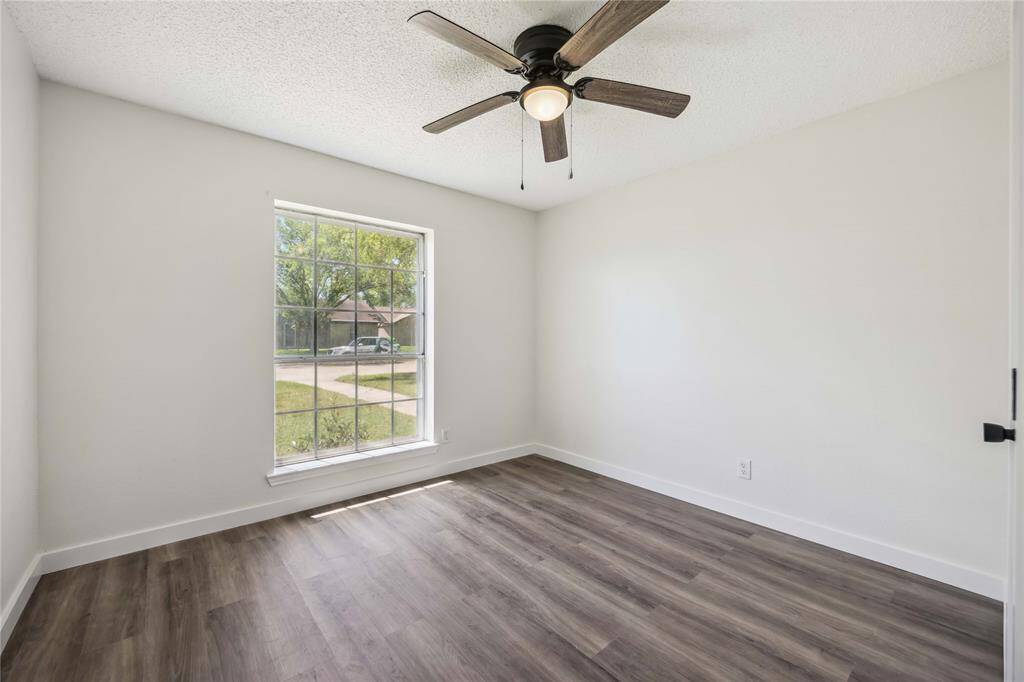 This room features a large window allowing plenty of natural light, a modern ceiling fan, and sleek wood flooring, creating a bright and welcoming atmosphere.