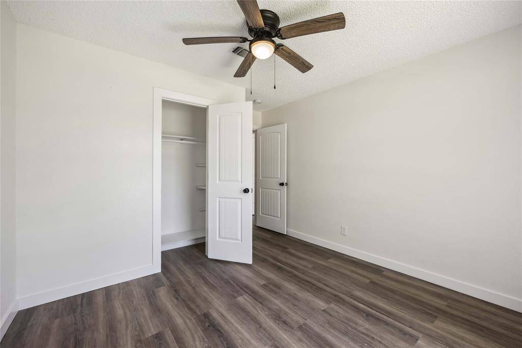This room features a neutral color palette with light walls and wood-style flooring. It includes a ceiling fan and a spacious closet with white double doors, offering a clean and modern look.