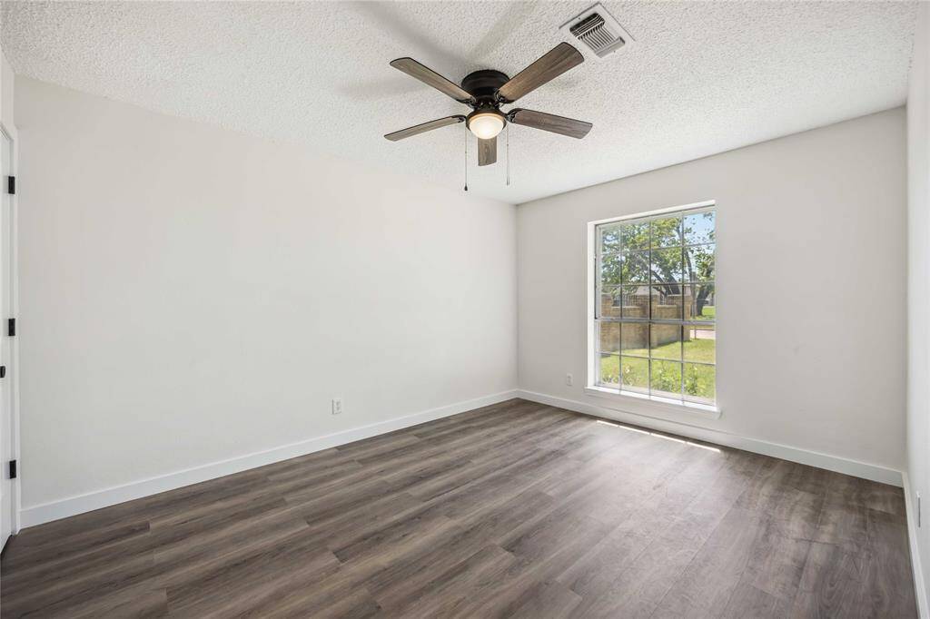 Bright, airy bedroom with wood flooring, a ceiling fan, and a large window providing natural light.