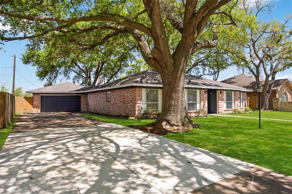 Charming brick home with a spacious front yard featuring mature trees. It has a long driveway leading to a two-car garage. The property offers a welcoming, serene atmosphere.