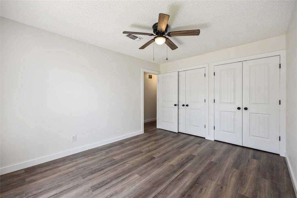 This photo shows a bright, spacious bedroom with light-colored walls and wood-style flooring. It features a ceiling fan and ample closet space with double doors, creating a clean and modern look.