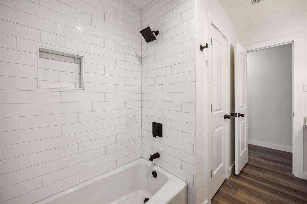 Modern bathroom featuring a white subway-tiled shower with a built-in niche and matte black fixtures. Adjacent hallway with wood flooring and white paneled doors.