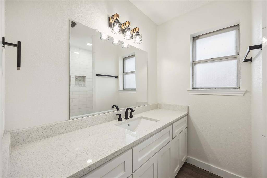 This bathroom features a modern design with a long white vanity, sleek black fixtures, and a large mirror. It includes a frosted window for natural light and privacy, complemented by a stylish light fixture.