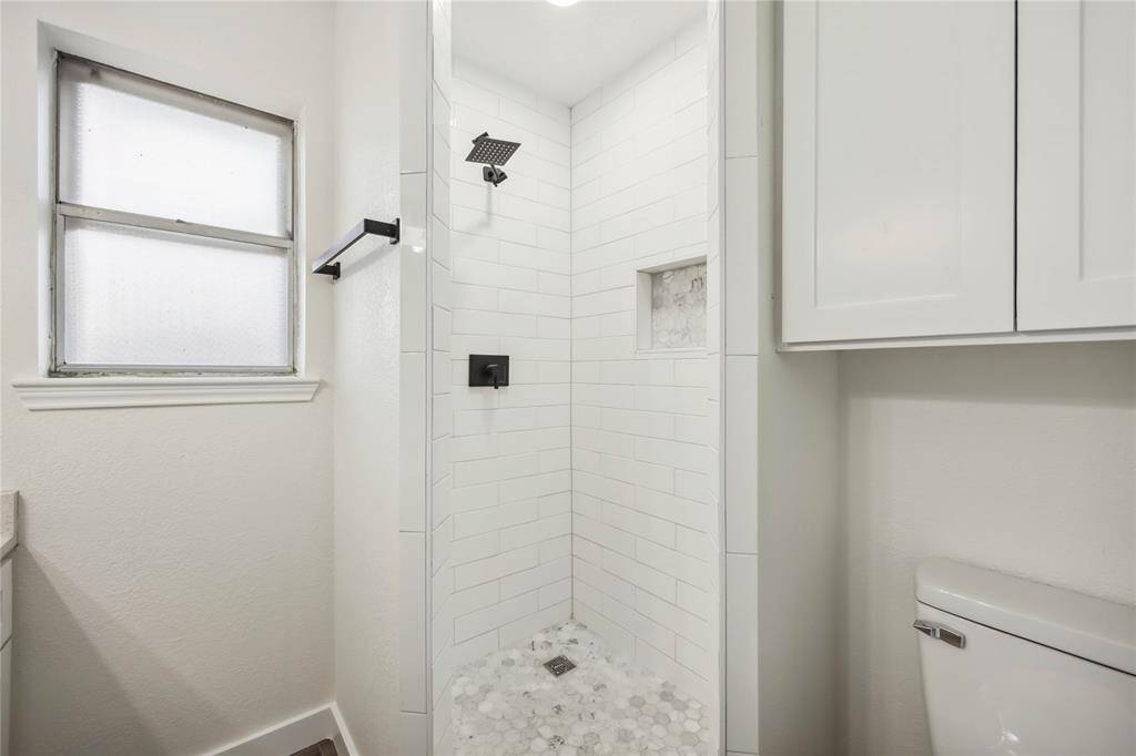 This bathroom features a modern shower with white subway tiles and a built-in niche, complemented by a sleek black showerhead. It has a frosted window for natural light and privacy, and white cabinetry for storage.