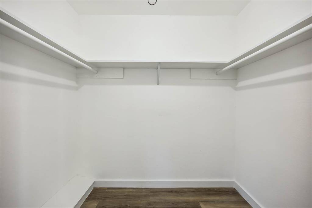 Spacious walk-in closet with white walls, dual hanging rods, and wood flooring, perfect for ample storage and organization.
