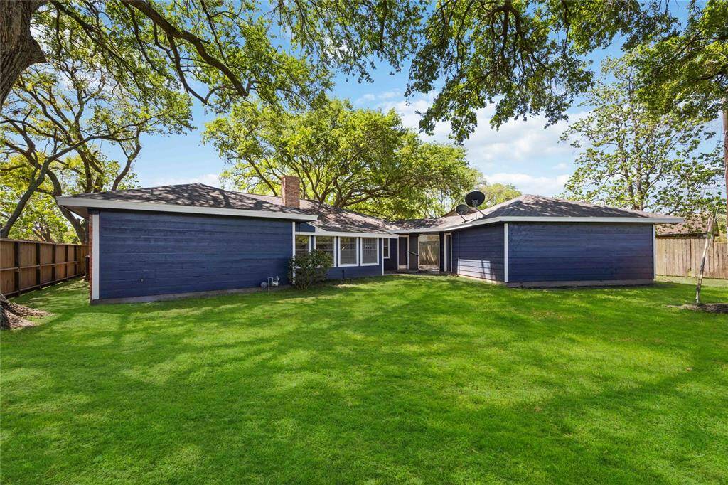 This photo showcases a single-story, dark blue house with a spacious, well-maintained backyard. The property is surrounded by a wooden fence and mature trees, providing privacy and shade. Ideal for outdoor activities and relaxation.
