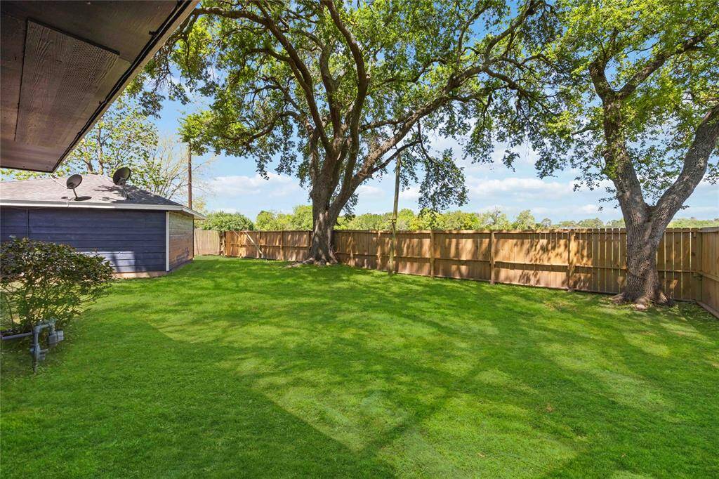 This photo showcases a spacious, well-maintained backyard with lush green grass and large shade trees. The area is enclosed by a wooden fence, offering privacy and a serene atmosphere, perfect for outdoor activities or relaxation.