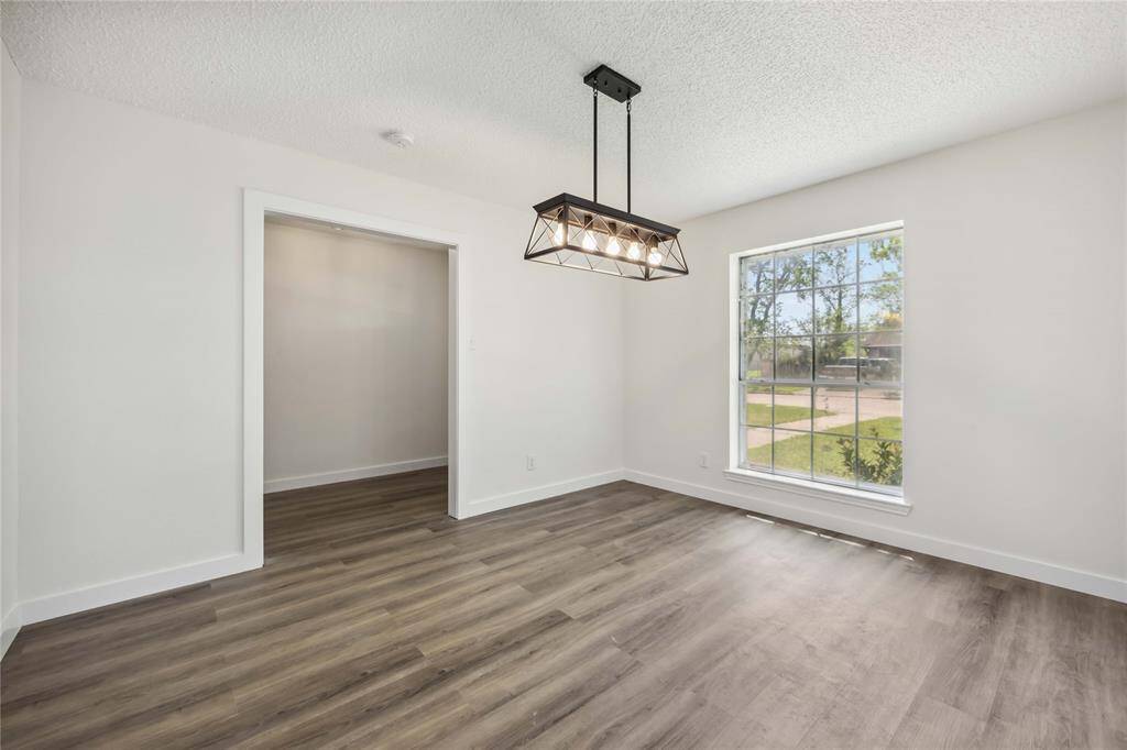 This room features a modern light fixture, large window with natural light, and stylish wood flooring, creating a bright and inviting space.