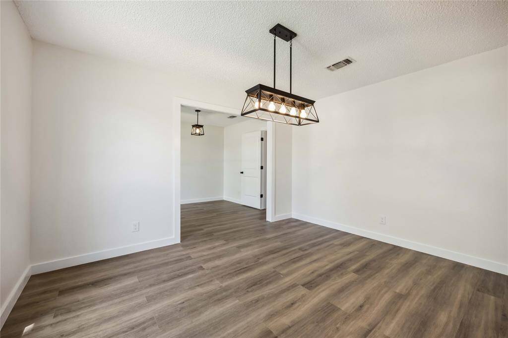 This room features a modern light fixture, fresh white walls, and wood-style flooring, offering a clean and contemporary look, perfect for a dining or living area.