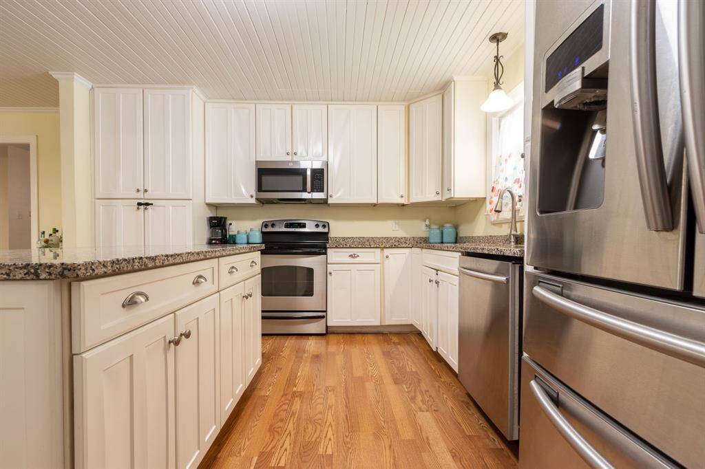 Kitchen island to the left. Refrigerator, double sink & dishwasher to the right. Range and microwave in the background.