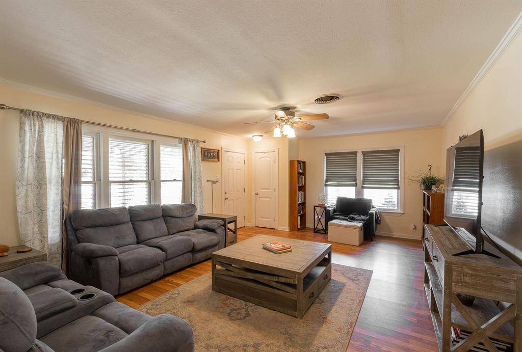 Large living room with front door in the background. Beautiful wood floors, crown molding and baseboards.
