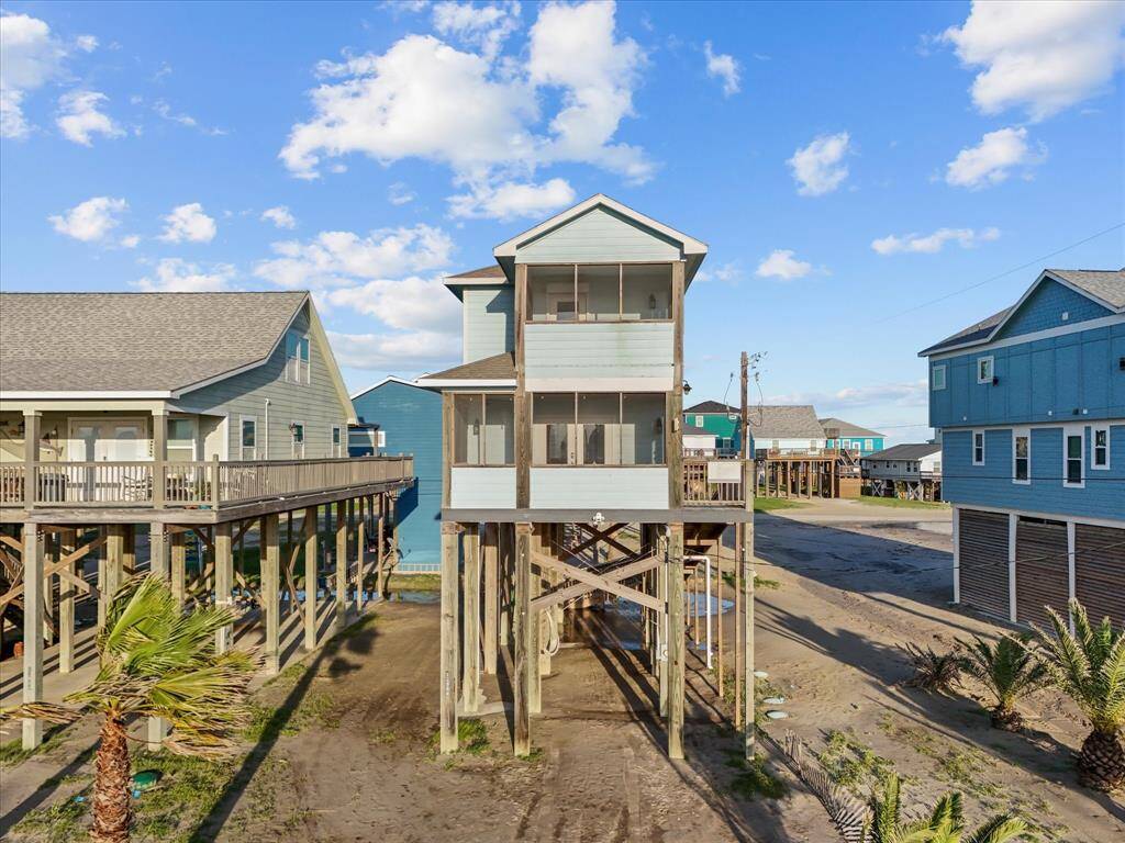 Elevated beach house with a light blue exterior, offering ocean views and a screened porch. The stilt design provides protection from high tides, while the sandy surroundings add a coastal charm. Ideal for a seaside lifestyle.