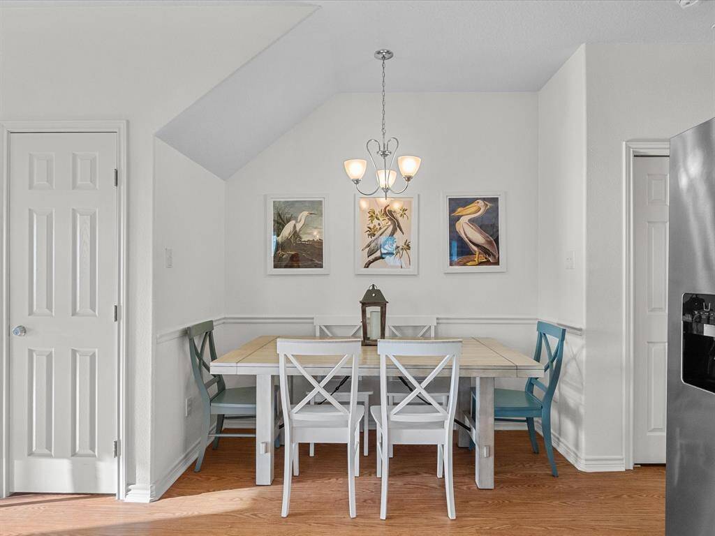 This cozy dining area features a wooden table with mismatched chairs, a modern chandelier, and bird-themed wall art. The space is bright with natural light, and has a warm, inviting atmosphere.