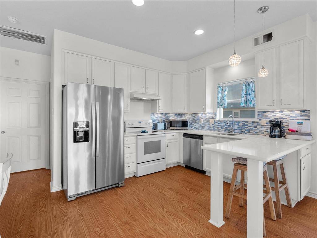 Bright, modern kitchen with stainless steel appliances, white cabinetry, and a stylish blue tile backsplash. Features a central island with bar seating and hardwood look flooring.