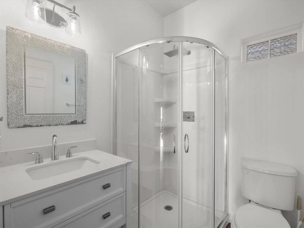This modern bathroom features a sleek glass-enclosed shower, a stylish vanity with a marble countertop, and contemporary lighting. The white walls and fixtures create a bright and clean aesthetic.