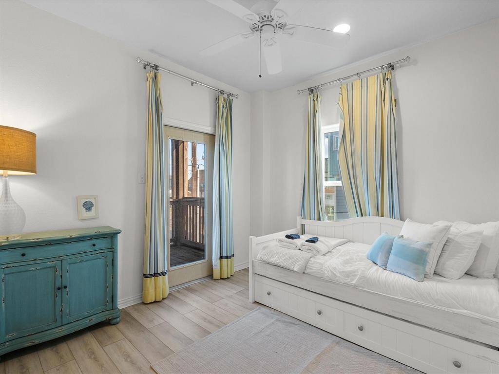 This cozy bedroom features a daybed with storage drawers, a vintage-style turquoise dresser, and a ceiling fan. The room is bright, with striped curtains and a glass door leading to a small balcony, creating a welcoming and airy atmosphere.