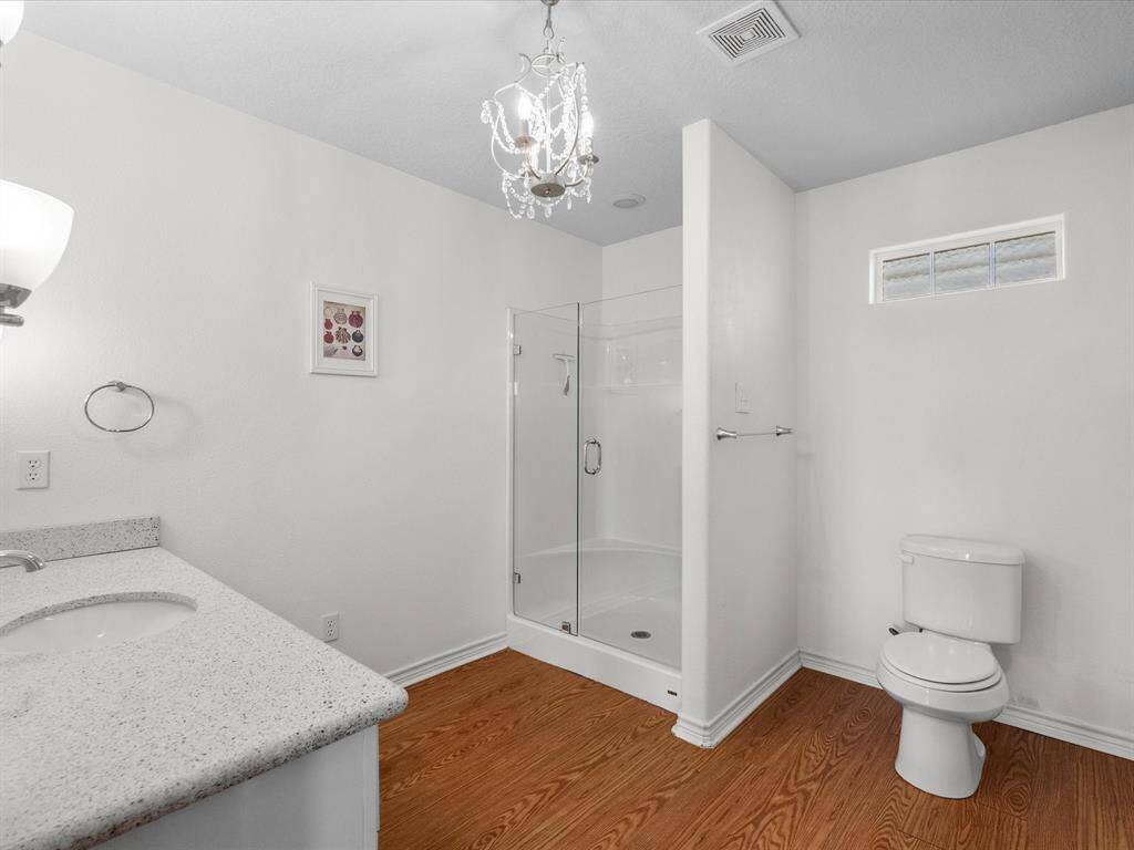Bright and spacious bathroom featuring a glass-enclosed shower, elegant chandelier, modern fixtures, and wood-look flooring, offering a clean and stylish design.