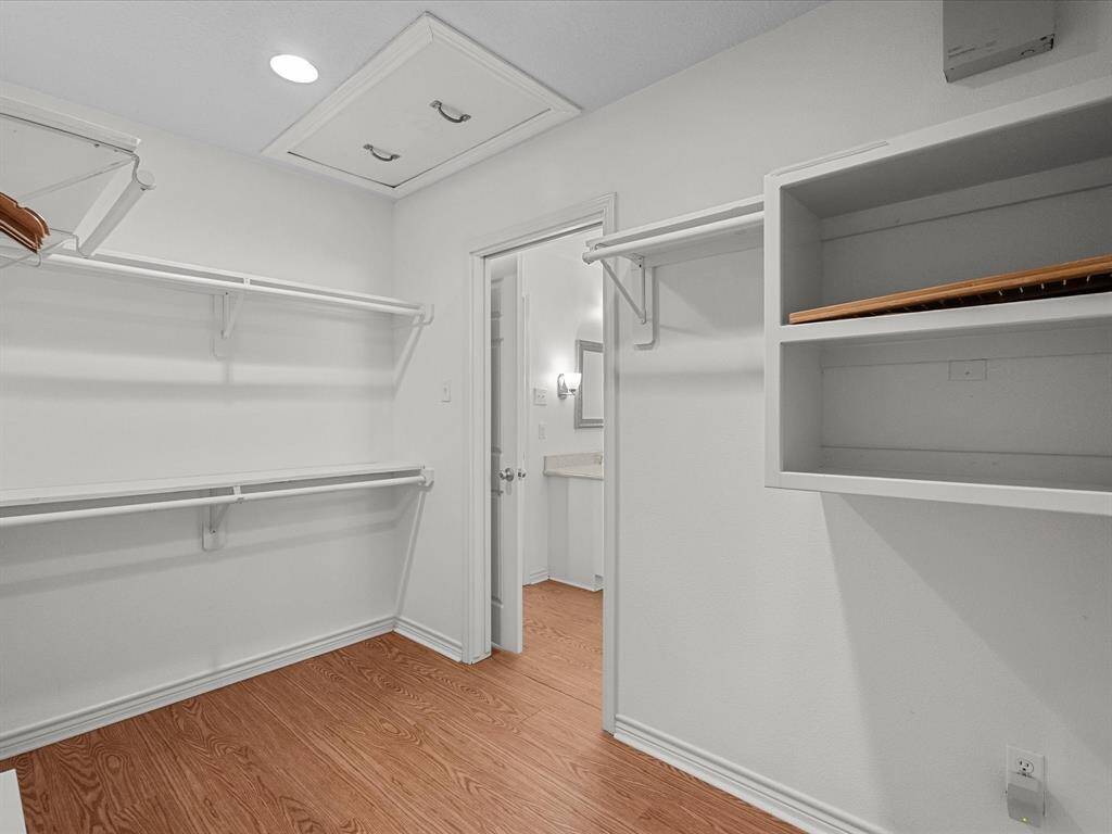 This photo shows a spacious walk-in closet with wooden look flooring, ample shelving, and hanging space. It connects to a bathroom, providing convenience and accessibility.
