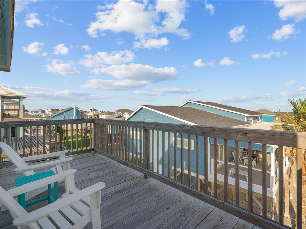 Spacious wooden deck with seating, offering a scenic neighborhood view and bright blue skies. Ideal for relaxation and outdoor enjoyment.