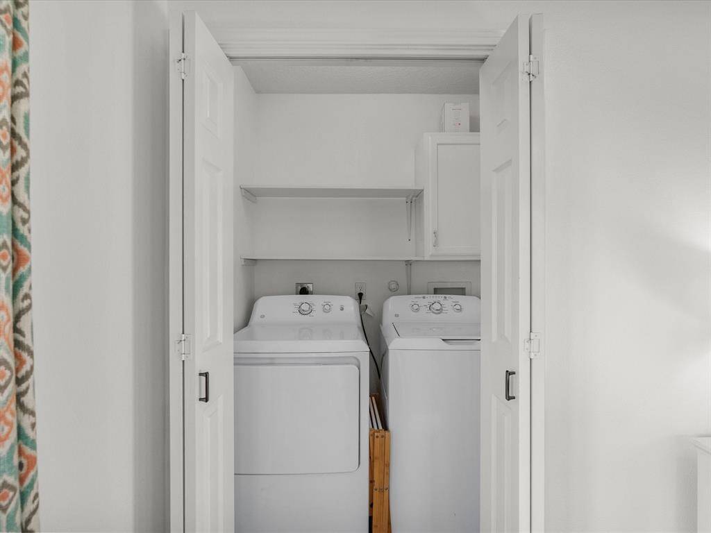This photo shows a compact laundry area with a washer and dryer neatly fitted into a closet space, featuring white folding doors and a shelf above for storage.