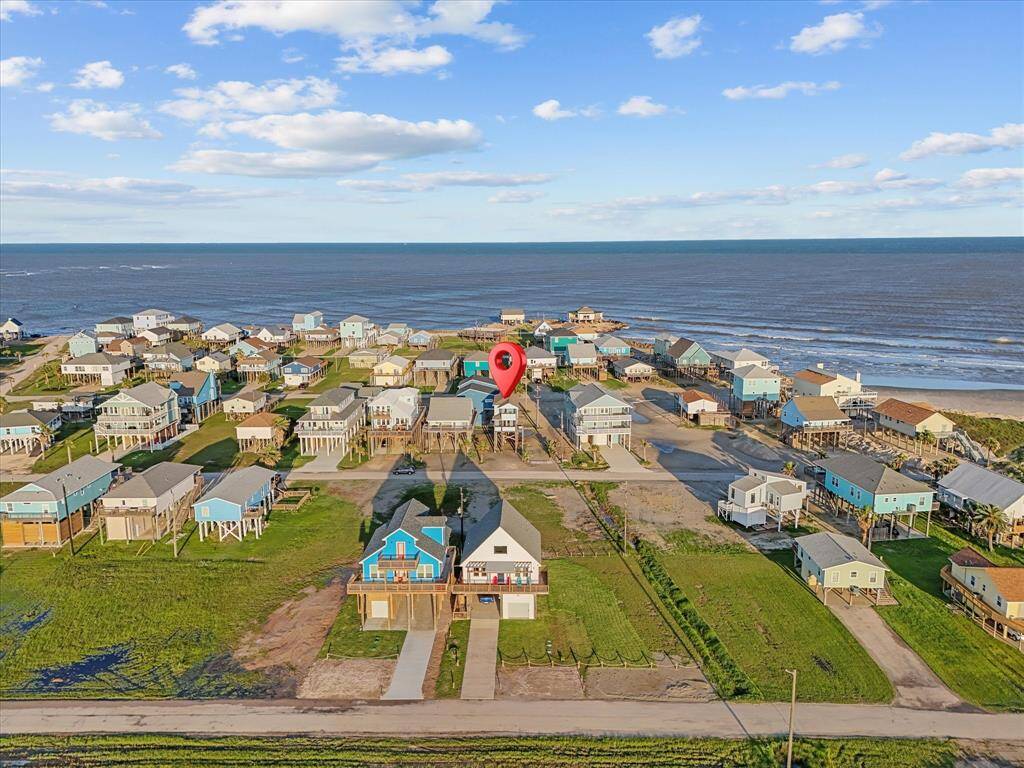 This aerial photo showcases a coastal neighborhood with charming homes, many elevated on stilts, offering beautiful ocean views. The area appears peaceful and well-maintained, with close proximity to the beach, making it an ideal spot for seaside living.