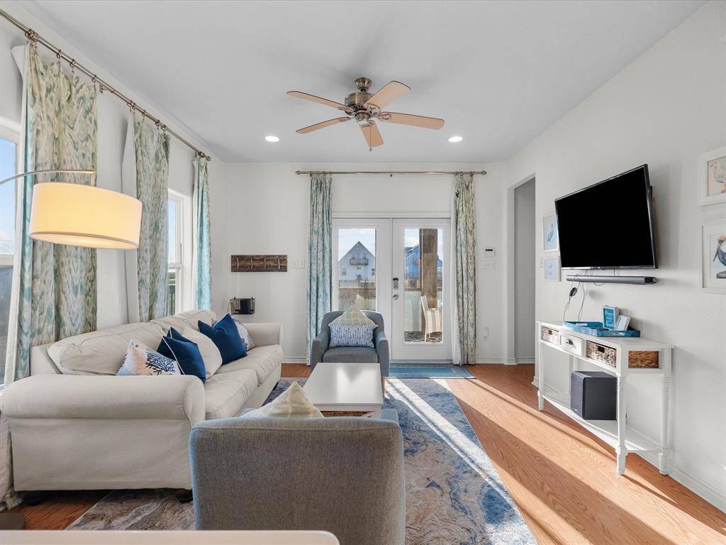 Bright and inviting living room with natural light, featuring hardwood floors, a ceiling fan, and a wall-mounted TV.