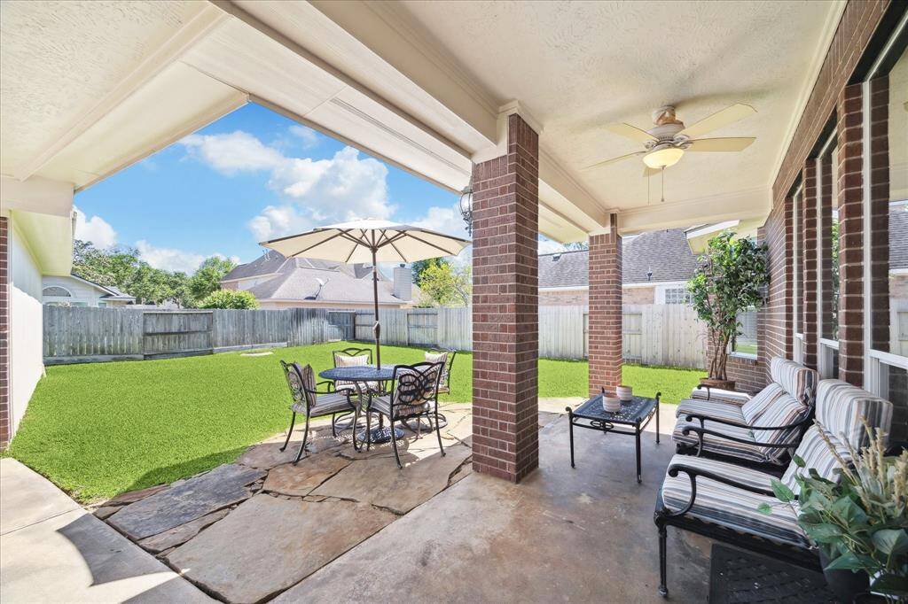 COVERED PATIO WITH CEILING FAN OVERLOOKING THE SPACIOUS BACKYARD.