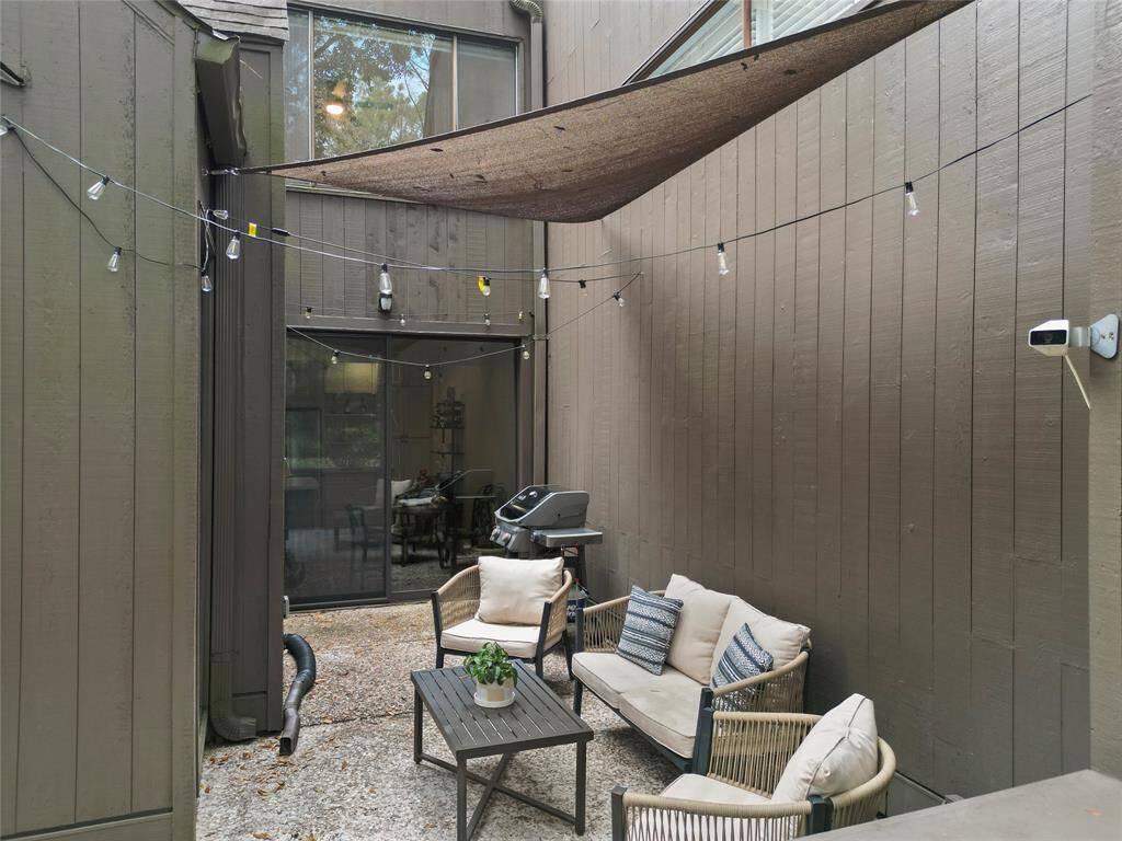 This charming outdoor patio offers a cozy seating area, perfect for unwinding or gathering with friends. Twinkling string lights and a serene tree-lined backdrop create a private, inviting retreat.