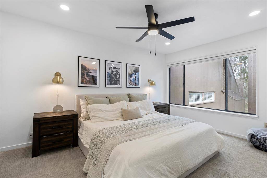 This photo showcases a spacious primary bedroom with a neutral color palette. Note the large window and modern fan!