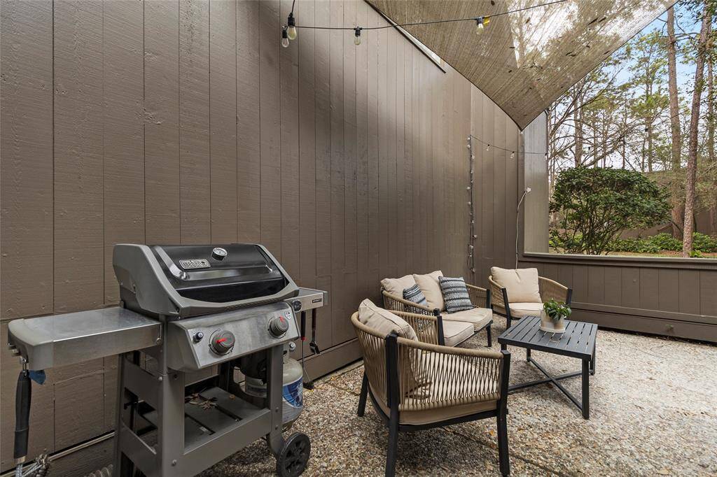 This cozy outdoor patio offers a private retreat with a warm, inviting atmosphere. Surrounded by wood-paneled walls and illuminated by overhead string lights, it provides the perfect space for relaxing or gathering with loved ones.