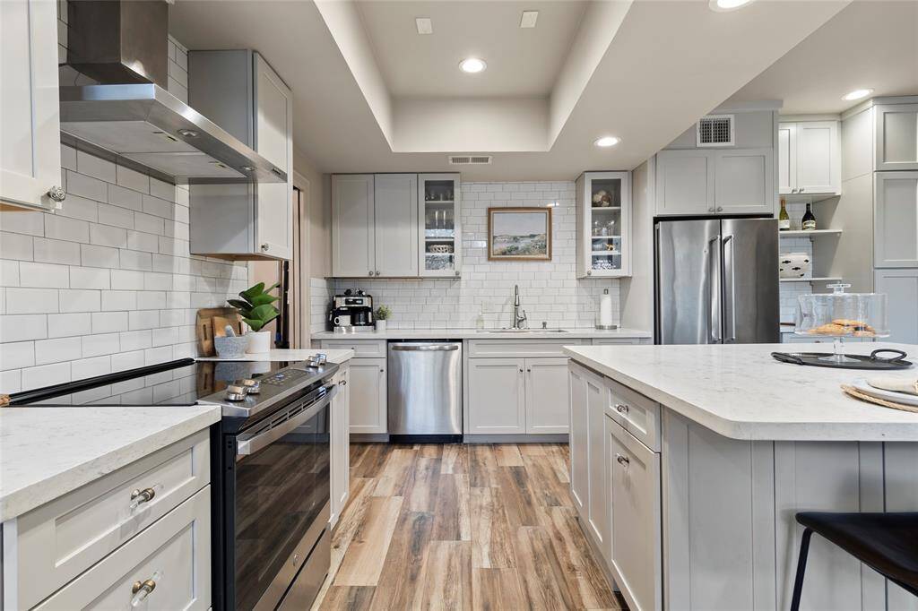 This modern kitchen boasts a spacious island with seating, stainless steel appliances, and sleek white cabinetry. Flowing into a spacious living area and bright outdoor patio, it provides the perfect space for entertaining.