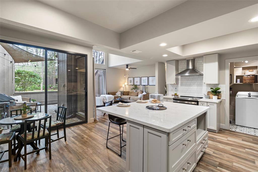This modern kitchen features sleek white cabinetry, stainless steel appliances, and a spacious island with bar seating. The wood-look flooring adds warmth, while recessed lighting ensures a bright, inviting space. Ideal for entertaining, there's also a cozy dining nook.