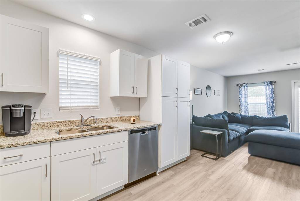This photo showcases a bright and open kitchen and living area. The kitchen features granite countertops, white cabinetry, and stainless steel appliances. The adjacent living space includes a large, comfortable sectional sofa and ample natural light from multiple windows.