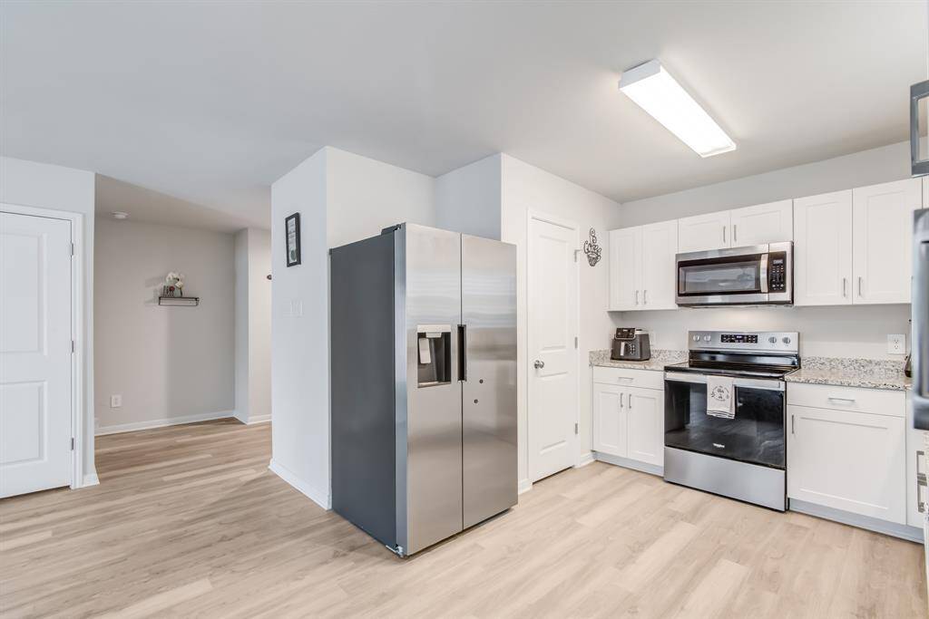 Modern kitchen with sleek stainless-steel appliances, white cabinetry, and like wood flooring. It features granite countertops and ample storage, creating a clean and inviting space.