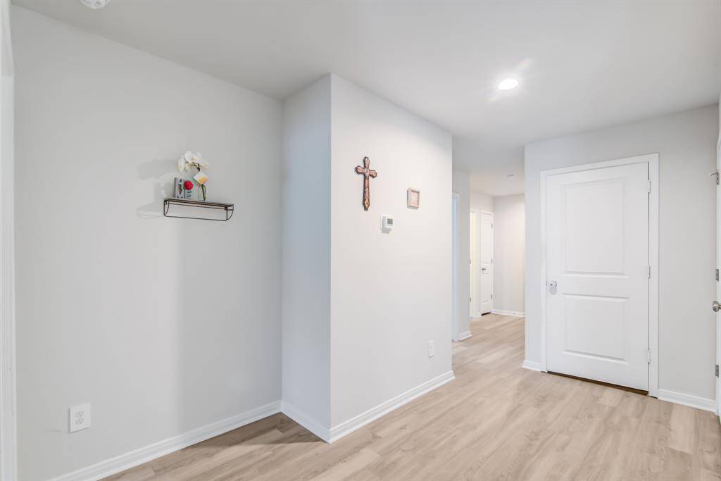 This hallway features like wood flooring and neutral walls, offering a clean and bright entrance.  The area is well-lit with recessed lighting, leading to multiple rooms and the door leading to the garage.