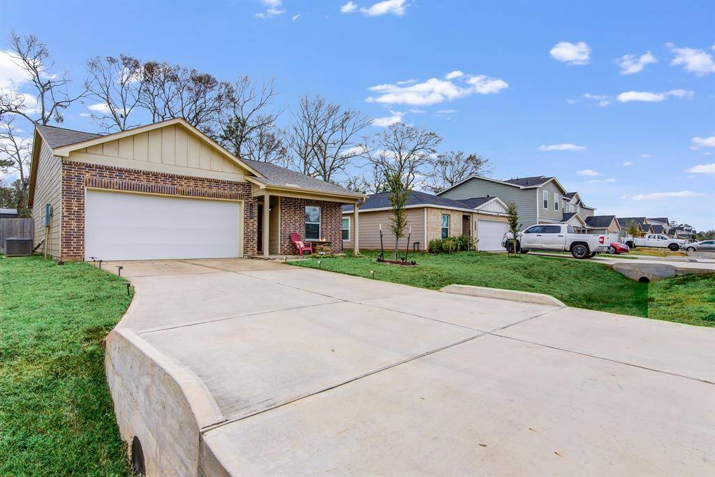 This photo shows a single-story brick home with a spacious driveway and a two-car garage. The front yard is neatly landscaped, and the house features a small porch area. The neighborhood appears quiet and well-maintained.