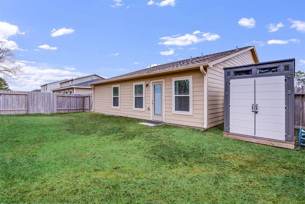 This photo shows a cozy backyard with a well-maintained lawn, fenced for privacy, and features a small shed that will stay with the home.  The house has a back door leading to the yard.