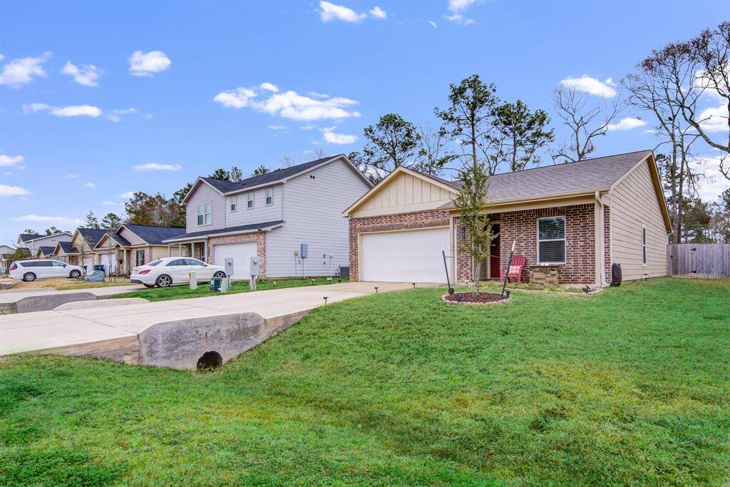This photo shows a charming single-story brick home with a two-car garage, set on a well-maintained lawn. The neighborhood features similar homes and is lined with trees, creating a welcoming country atmosphere.
