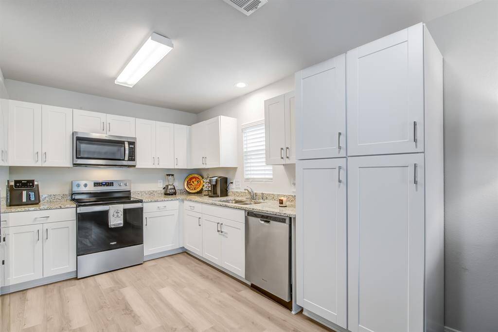 This modern kitchen features sleek white cabinetry, stainless steel appliances, and wood like flooring. It has ample counter space with a clean, bright design.