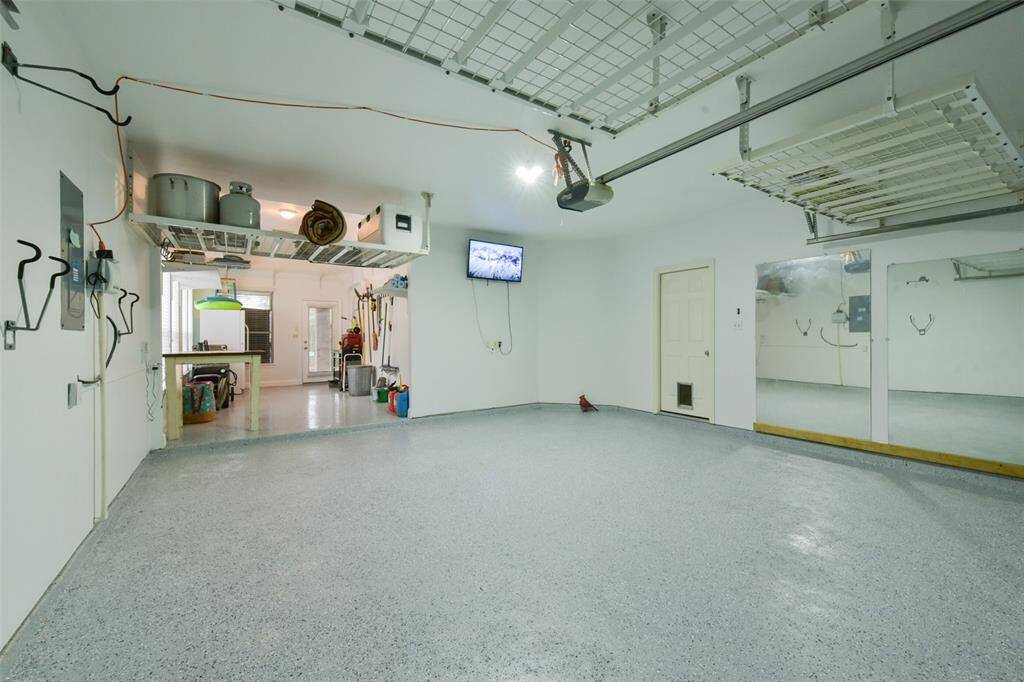 Three-car tandem garage with door that leads to the backyard. Also notice the recent epoxy flooring as well as the hanging storage.