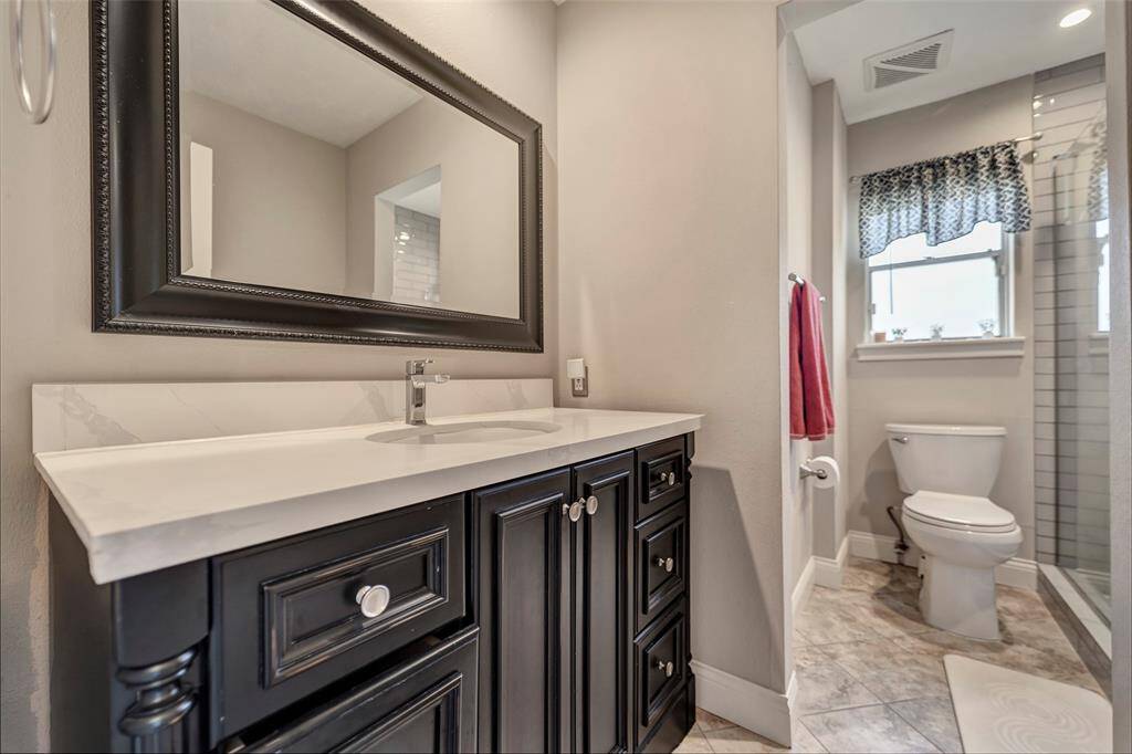 The secondary bathroom has been recently updated with custom cabinetry, quartz countertops, and a framed mirror.