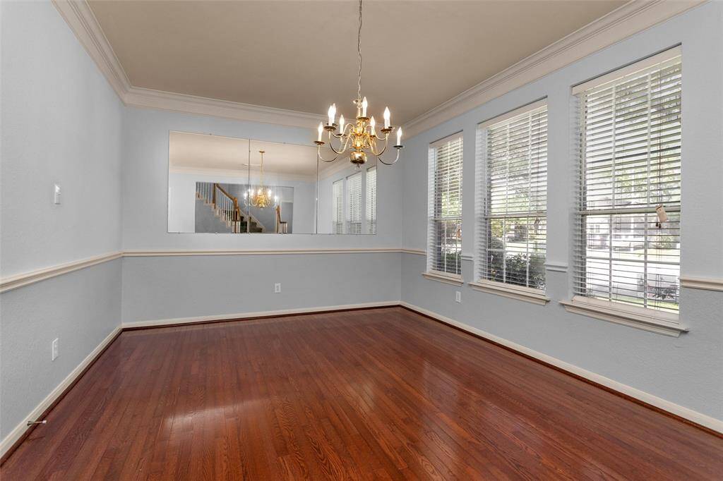 Elegant dining room featuring rich hardwood floors, abundant natural light from large windows, and a stylish chandelier. Perfect for hosting gatherings and creating memorable meals.