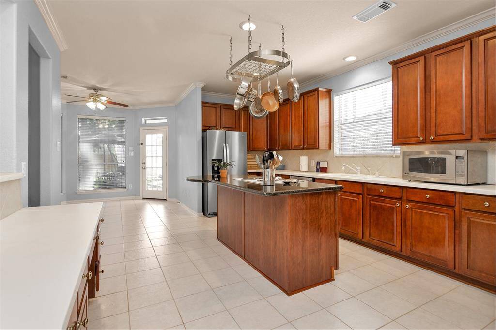Spacious and elegant kitchen featuring rich wooden cabinetry, a central island with sleek countertops, and modern stainless steel appliances. Ideal for culinary enthusiasts and entertaining guests.